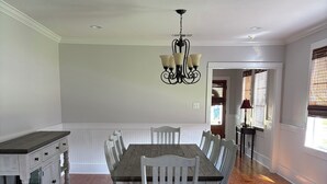 A dining area with a wooden table and chairs, a chandelier, and a view of the adjacent room. - Spacious 5-bedroom house in charming Bay St. Louis with WiFi, AC (Bay St. Louis)