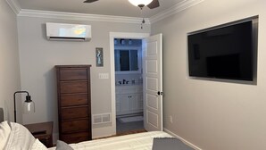 A bedroom with a bed, a dresser, a ceiling fan, a TV, and an open door to a bathroom. - Spacious 5-bedroom house in charming Bay St. Louis with WiFi, AC (Bay St. Louis)