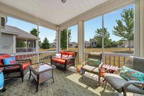 A covered patio with wicker furniture, a glass table, and a view of neighboring houses. - The Catbird - 28 Butternut (Prince Edward)