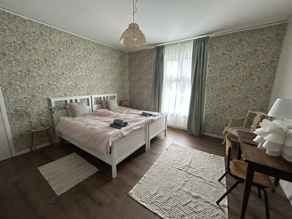 A bedroom with a bed, a desk, a chair, a lamp, and a hanging light fixture.