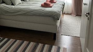 Un lit bien fait, avec des oreillers et une serviette pliée, un tapis à rayures et un motif floral sur le papier peint.