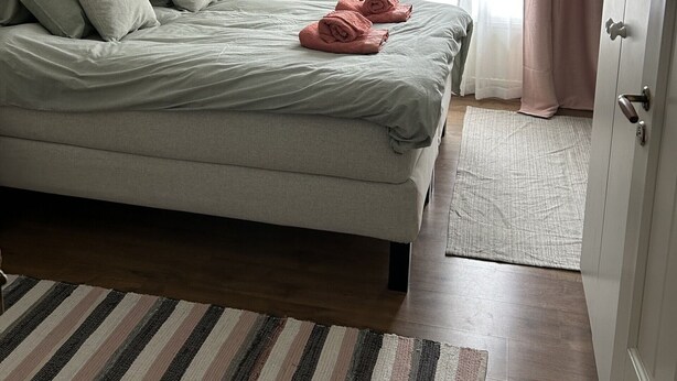 Un lit bien fait, avec des oreillers et une serviette pliée, un tapis à rayures et un motif floral sur le papier peint.