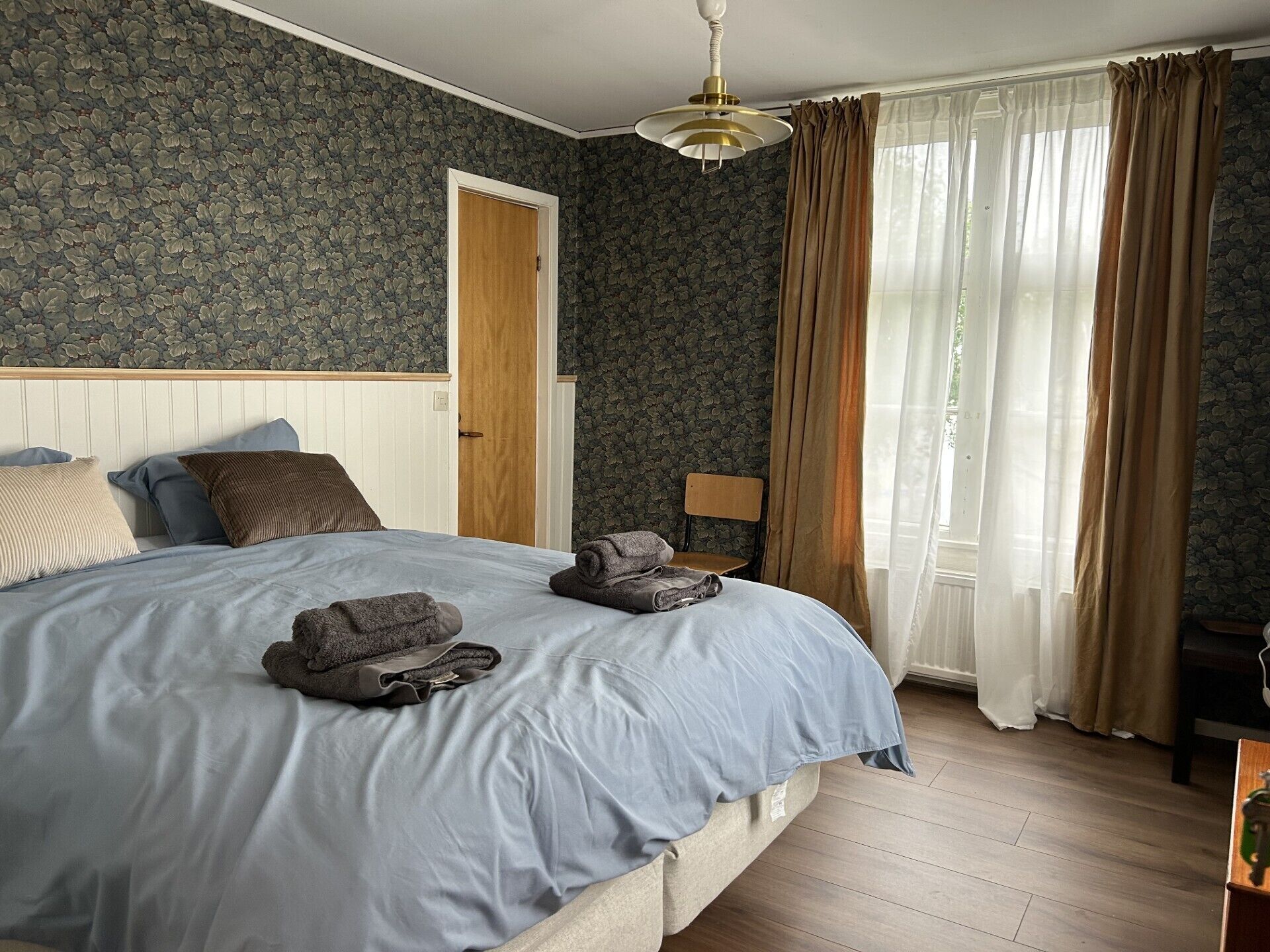 A bedroom with a bed, a chair, a wooden door, and a window with curtains.