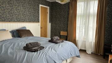 A bedroom with a bed, a chair, a wooden door, and a window with curtains.