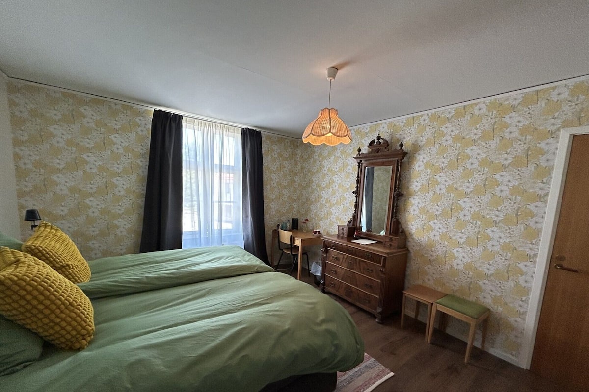 A bedroom with a bed, a dresser, a mirror, a desk, and a bench.