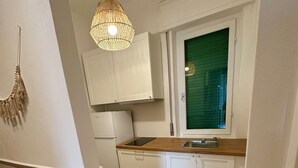 A kitchen with white cabinets, a wooden countertop, a hanging light fixture, and a window with blinds. - Domoi Property Apartment (Pisa)