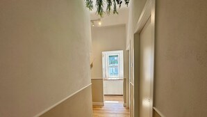 A narrow hallway with wooden flooring and white walls, leading to a kitchen area with white cabinets and a window with a view. - Domoi Property Apartment (Pisa)