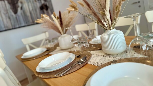 A dining table set with white plates, silverware, and a vase with dried pampas grass. - Domoi Property Apartment (Pisa)