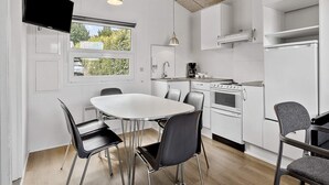 A modern kitchen with white cabinets, a dining table with chairs, and a TV mounted on the wall. - 8 Person Holiday Park Home in Faaborg (Faaborg)