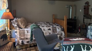 Una habitación acogedora con una cama, una silla, una mesa con una manta, una lámpara y una chimenea.