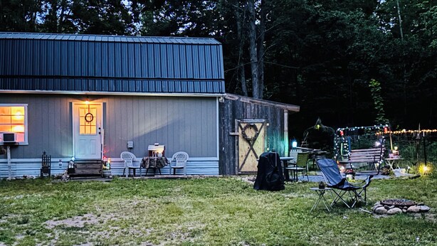 Una cabaña rústica con techo de metal, una puerta principal y un pequeño porche con dos sillas y una mesa.
