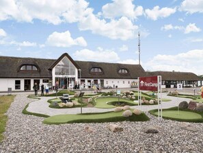 A building with a thatched roof, a reception area, and a landscaped garden with a golf course model. - 6 Person Holiday Park Home in Fjerritslev (Fjerritslev)