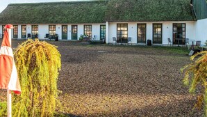 A building with a green roof and multiple windows, surrounded by a gravel courtyard with outdoor seating. - 2 Person Holiday Park Home in Fano (Fano)