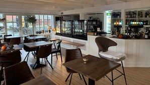 A restaurant with wooden tables and chairs, a bar area with bottles, and a view through large windows. - 2 Person Holiday Park Home in Fano (Fano)