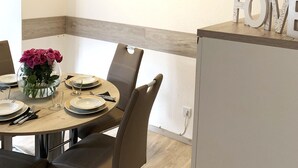A dining area with a round table set for four, a vase of pink roses, and a framed coastal landscape painting above. - Spacious Flat Near Hiking Trails (Winterberg)
