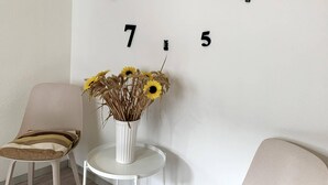 A room with two chairs, one with a striped cushion and another with a solid color. A white vase with dried flowers and sunflowers is on a small table. The wall has numbers '7' and '5' visible. - Spacious Flat Near Hiking Trails (Winterberg)