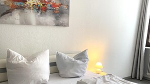 A neatly made bed with white bedding and pillows, a bedside lamp, and a colorful abstract painting on the wall. - Spacious Flat Near Hiking Trails (Winterberg)