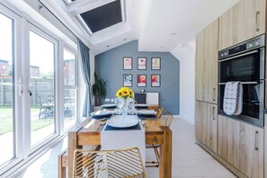 A modern kitchen with a dining area, large windows, and a view of the outdoors.