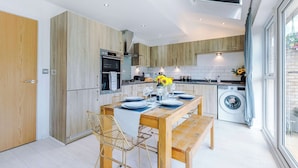 A modern kitchen with wooden cabinetry, a dining area with a table set for four, and a built-in washing machine. - Perfect Riverside Home in Manchester, FREE Parking (Manchester)