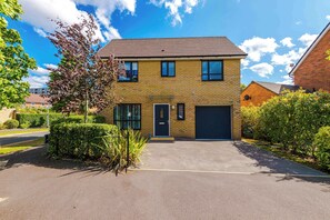 A two-story brick house with a garage, surrounded by well-maintained hedges and a clear sky.