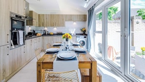 A modern kitchen with wooden cabinets, a built-in oven, and a dining area with a table set for six. - Perfect Riverside Home in Manchester, FREE Parking (Manchester)