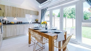 A modern kitchen with wooden cabinets, a dining table set for four, and large windows with curtains. - Perfect Riverside Home in Manchester, FREE Parking (Manchester)