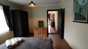 A bedroom with a bed, a dresser, a painting, and a hallway leading to a kitchen. - Emelys (Kumluca)