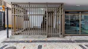 Une entrée sécurisée avec un portail en métal, un sol carrelé et une porte vitrée donnant sur un espace de stationnement.
