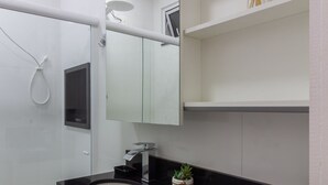 Une salle de bain moderne avec un plan de toilette noir, des meubles blancs, un grand miroir et une petite plante en pot.