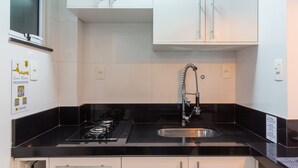 Une cuisine moderne avec des meubles blancs, un plan de travail noir, une cuisinière à gaz et un évier en acier inoxydable.