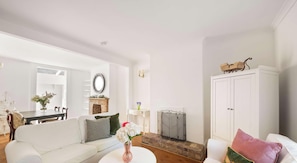 Una sala de estar con chimenea, muebles blancos y un espejo grande.