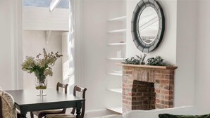 Un coin repas comprenant une table, des chaises, un vase de fleurs, une cheminée avec un manteau en briques et un miroir fixé au mur.