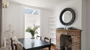 Un coin repas comprenant une table, des chaises, un vase de fleurs, une cheminée et un miroir au mur.
