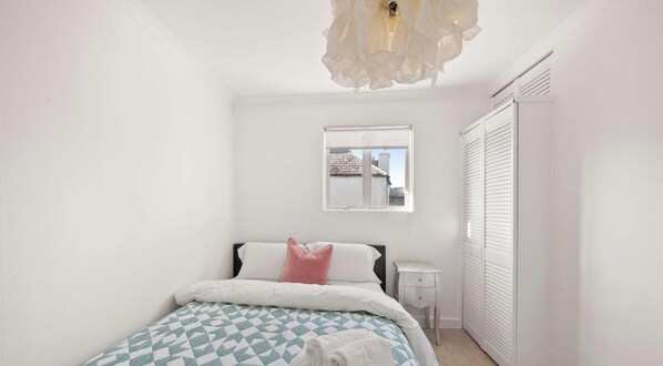 Een slaapkamer met een bed, nachtkastje, raam en kast.