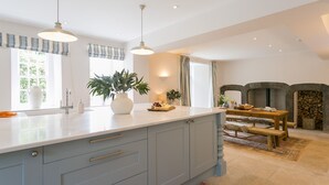 A modern kitchen with a large island, pendant lights, and a stone fireplace. - Treiorwerth -  a dog that sleeps 15 guests  in 7 bedrooms (Heart of Anglesey)