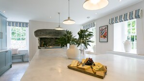A spacious kitchen with a central island, stone fireplace, large windows, and hanging pendant lights. - Treiorwerth -  a dog that sleeps 15 guests  in 7 bedrooms (Heart of Anglesey)