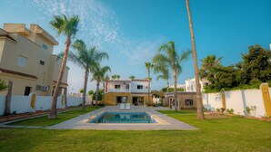 A pool surrounded by palm trees and a two-story building with a balcony. - Cabo negro villa with large garden, swimming pool and barbecue area (Cabo Negro)