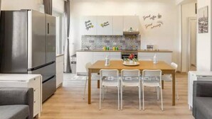 A modern kitchen with white cabinets, a stainless steel refrigerator, and a dining area with a wooden table and four chairs.