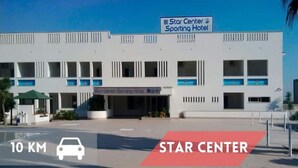 A modern hotel named Star Center Sporting Hotel with a clear sky and a sign indicating a 10 km distance.