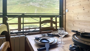 A dining table set with plates, cutlery, and a wine glass, with a view of green hills through a window. - (3.4344) Appartement 60m2 sur les pistes 3 Vallées (Les Menuires)