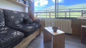 A cozy room with a sofa and a small table, large windows with a view of green hills and a clear sky. - (3.4344) Appartement 60m2 sur les pistes 3 Vallées (Les Menuires)