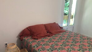 Ein Schlafzimmer mit einem gemusterten Bettbezug, einem Nachttisch aus Holz und einer Lampenschirm aus Weidengeflecht.