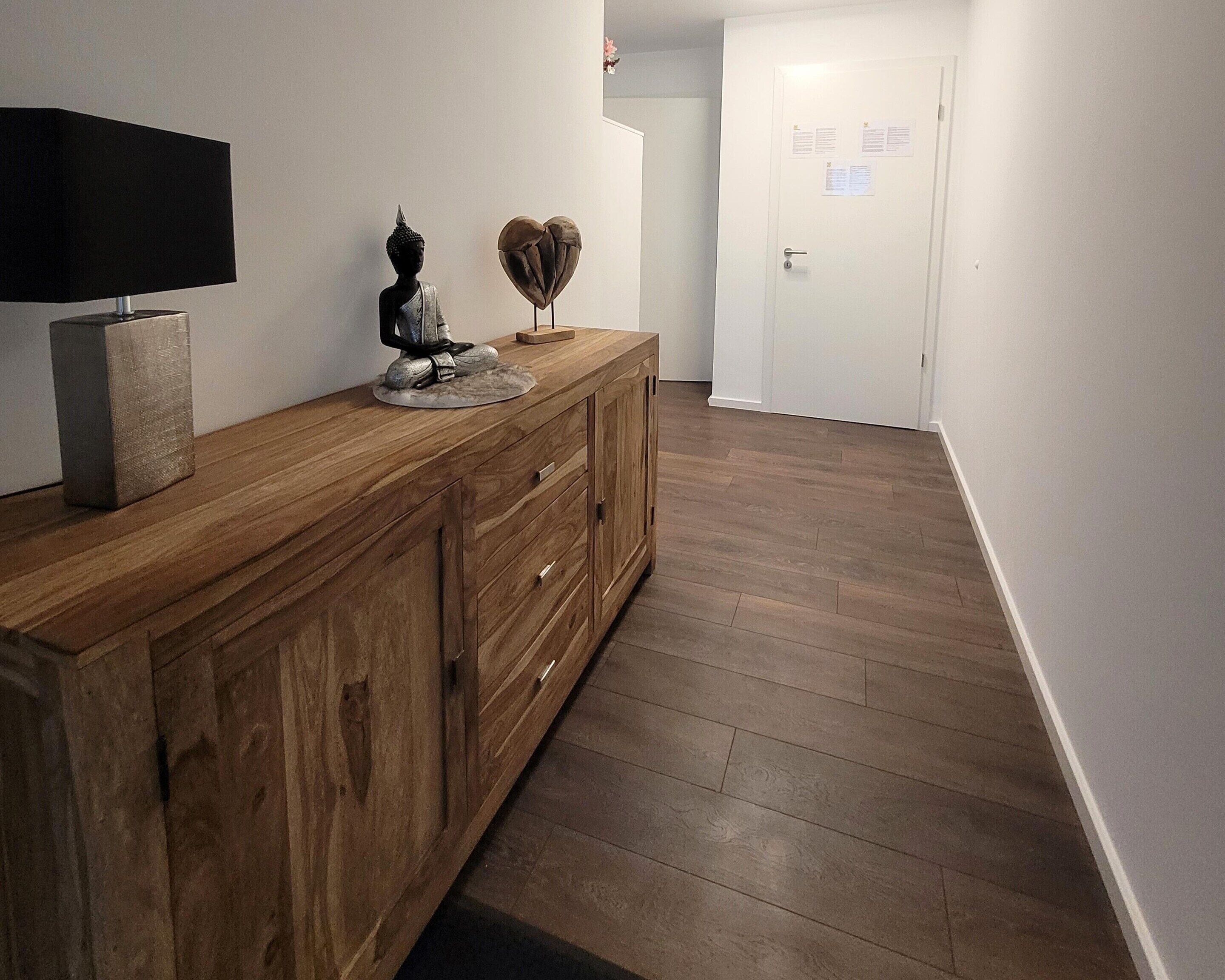 Een gang met een houten kast, een beeld en een hartvormige decoratie.
