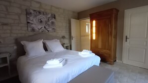A neatly made bed with white linens and towels, a nightstand with a lamp, a wall-mounted artwork, and a wooden wardrobe. - Toucan, 25m² air-conditioned room on first floor, separate entrance (Les Ulmes)