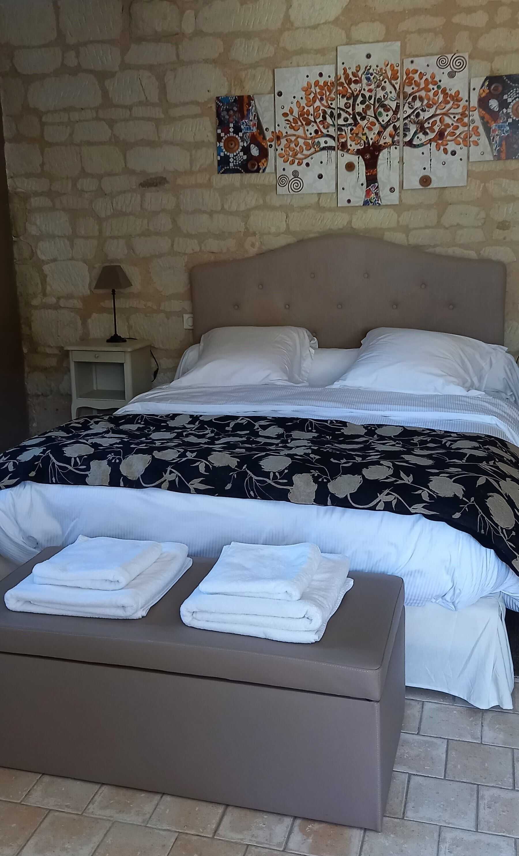 A bed with a floral-patterned bedspread, a headboard, and two folded white towels on a bench.