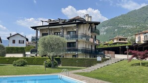 A multi-story building with balconies, a swimming pool, and a mountainous backdrop.
