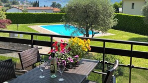 A balcony with a view of a swimming pool, a table with chairs, and a vase of flowers.