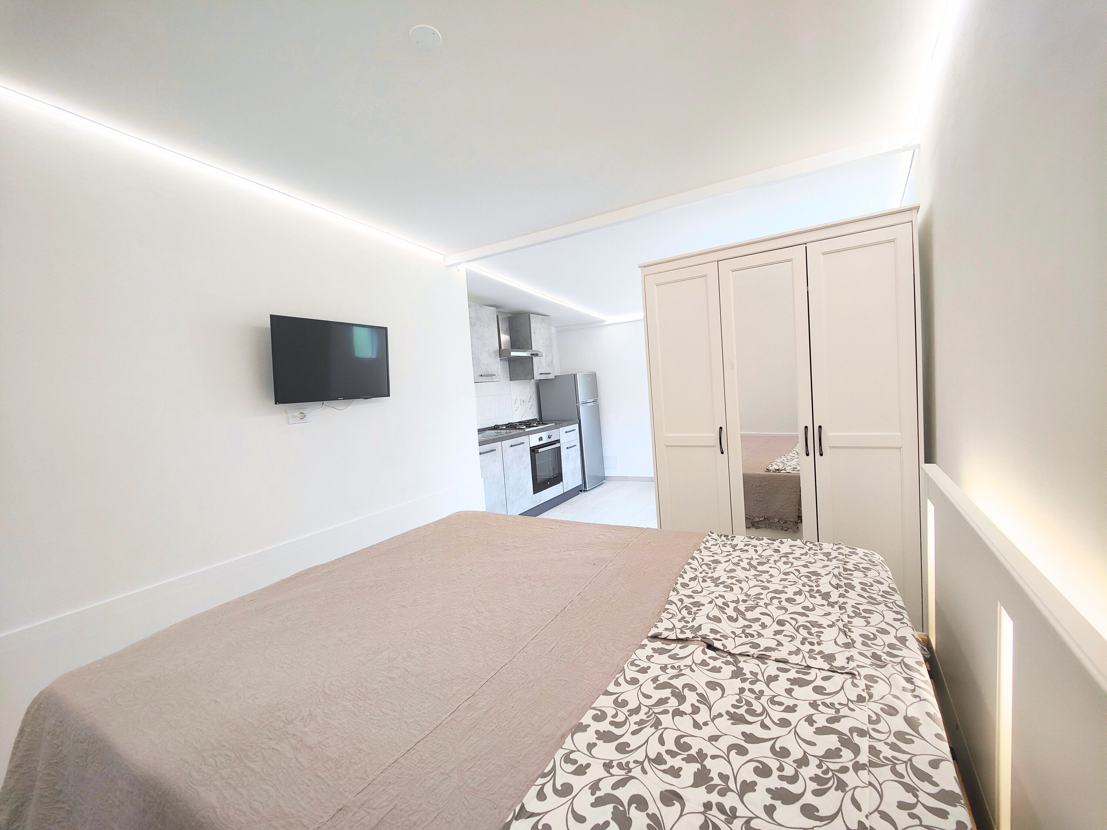 A bedroom with a bed, a TV mounted on the wall, and a wardrobe.