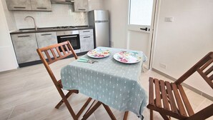 Una cocina compacta con electrodomésticos modernos, una mesa de comedor con sillas y una ventana con persianas.