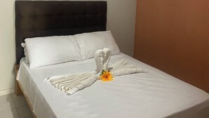 Un lit bien fait, agrémenté d’une serviette décorative et d’une fleur, un appareil de climatisation au-dessus, et un mur sobre.